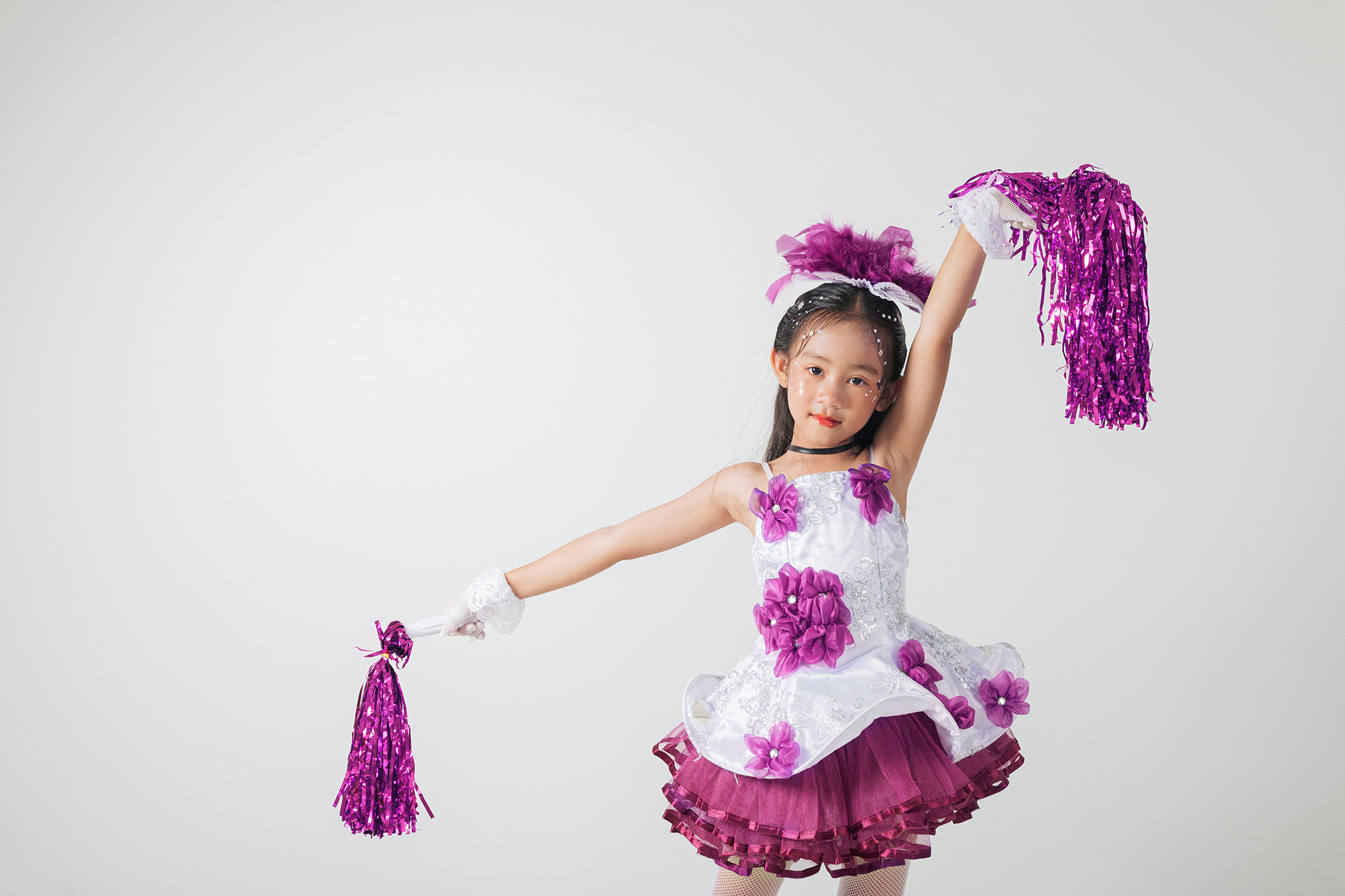 Portrait of a cheerful cheerleader girl in a purple and white outfit, holding purple pom-poms. Smiling brightly in a studio shot against a white background.